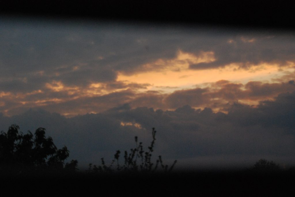 Photograph through a window frame showing the last of peach sunset light through lilac-grey clouds.