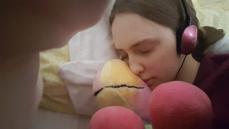 Sakara's head on her pillow, she's cugging a cuddly toy unicorn and looks cosy.