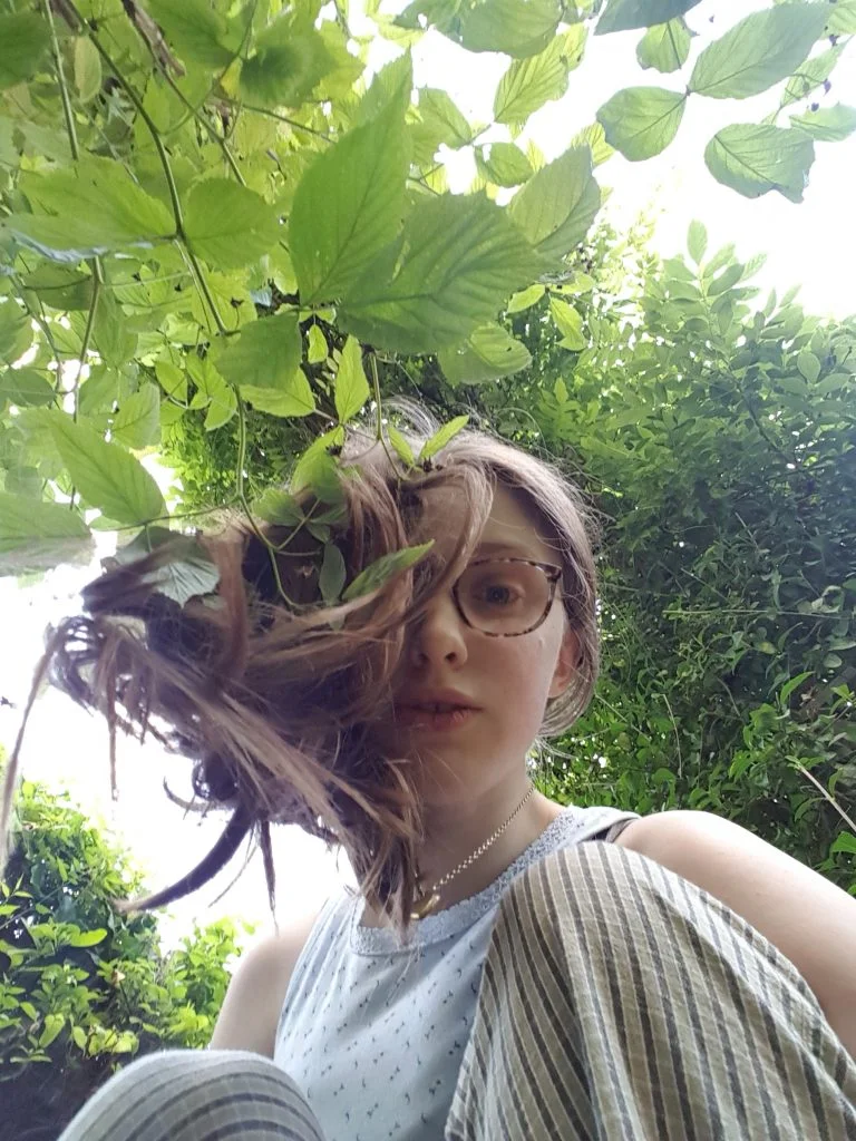 Sakara crouches down and half of her face is obscured by her hair falling forwards.
