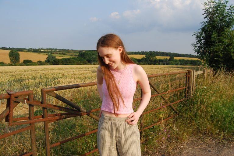 Sakara stands in front of a gate to a large field