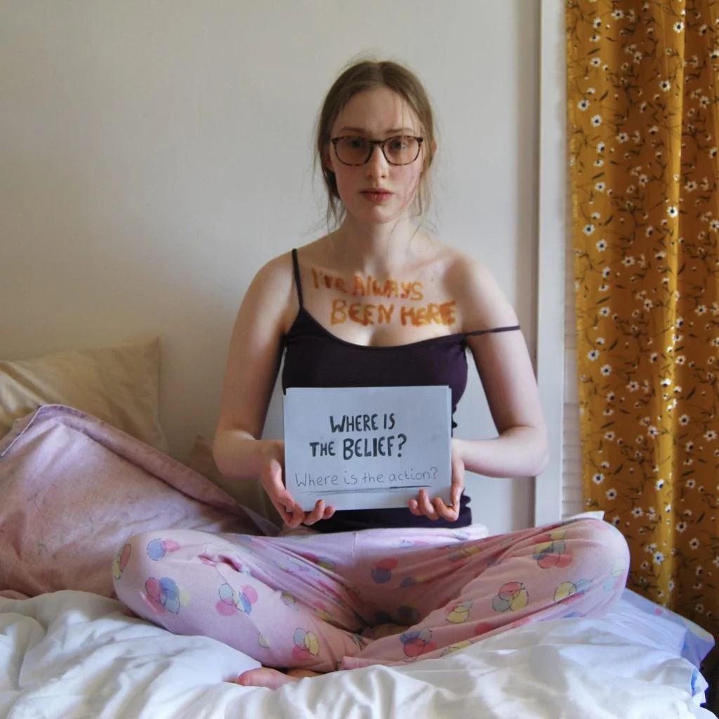 Sakara holds another sign asking two questions: where is the belief and where is the action?