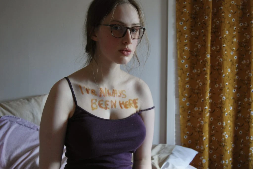One final photo of Sakara looking into the camera, not holding a sign but still with "I've always been here" written across her chest.