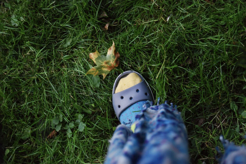 A foot wearing a sandal and sock next to a fallen leaf.