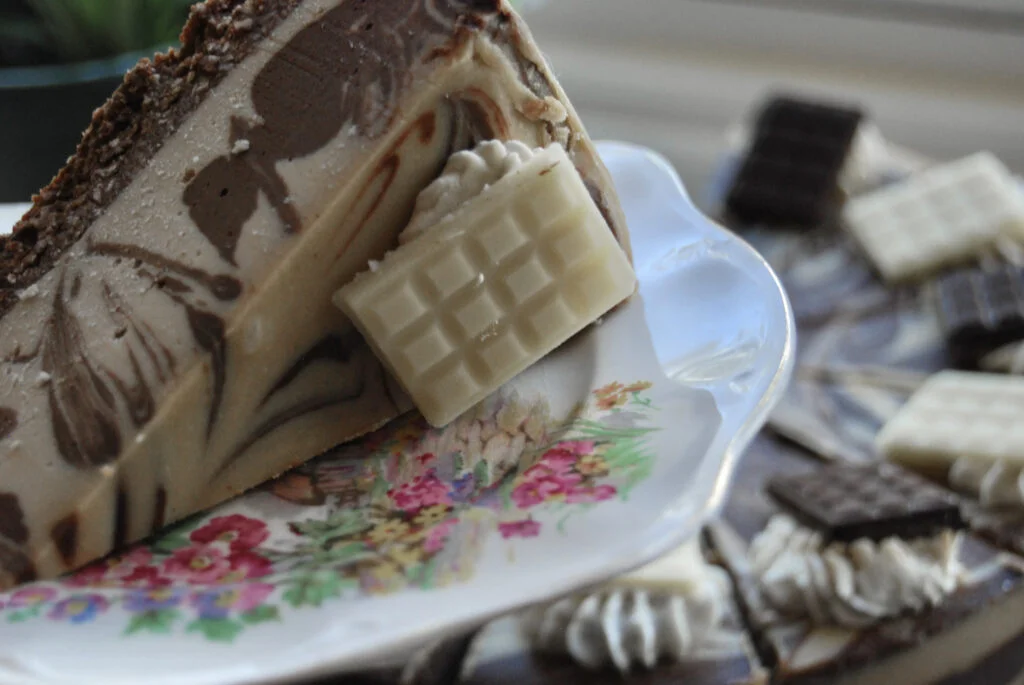 A slice of cake held on a plate held above the full round cake.