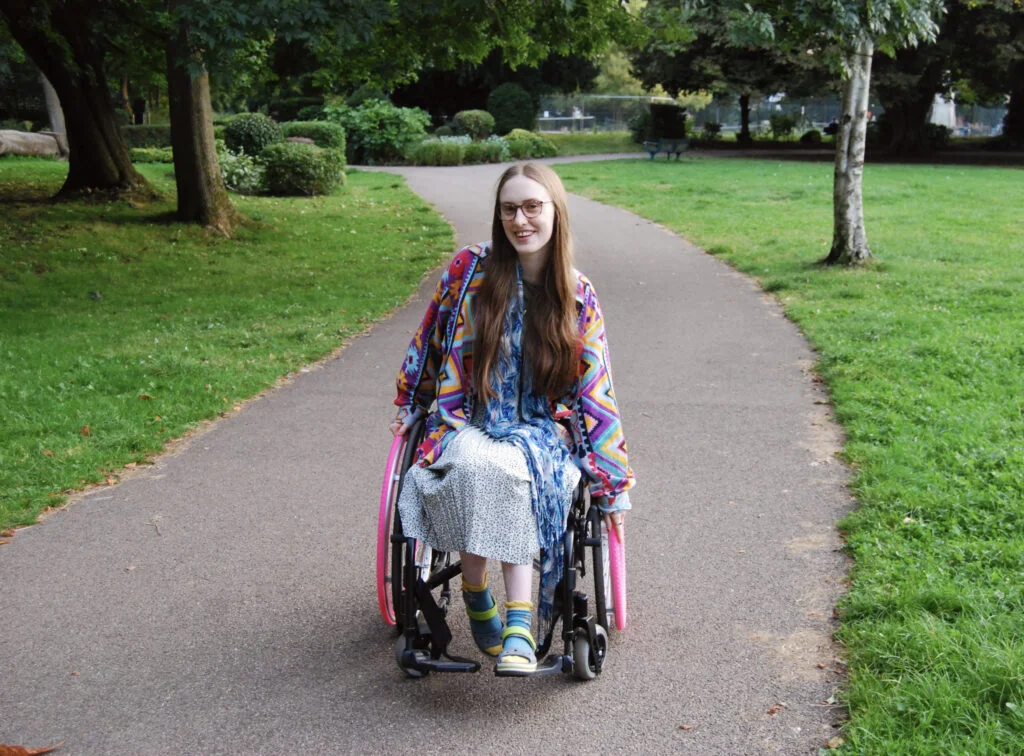 Another photo of Sakara in her wheelchair. She looks happy and is leaning to one side, pushing one wheel forwards.