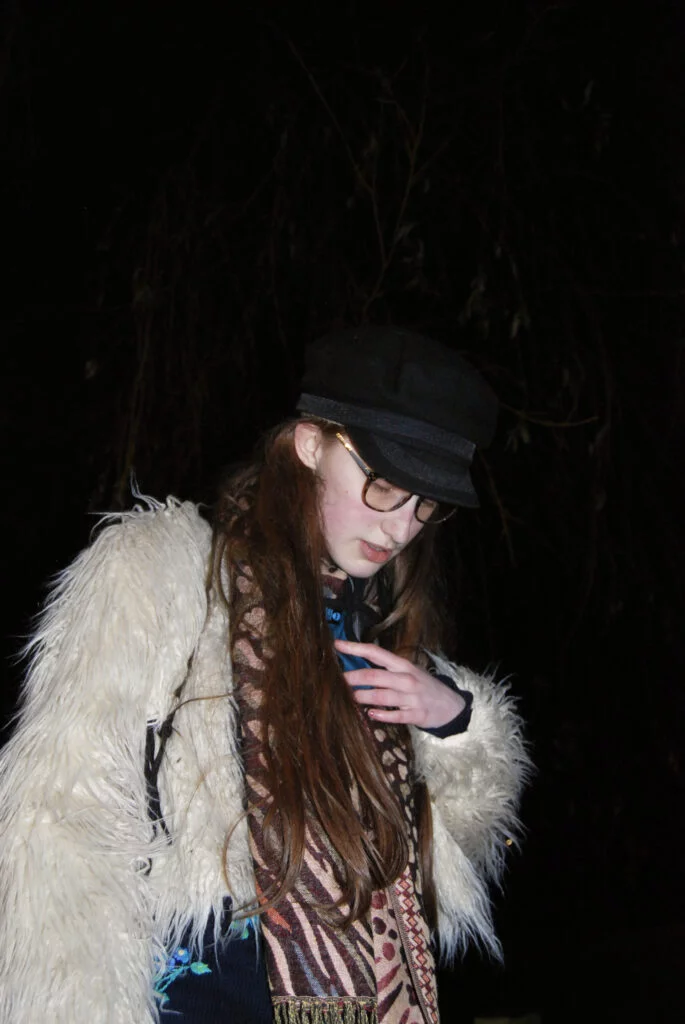Image: Sakara looks down. She wears a fluffy jacket.