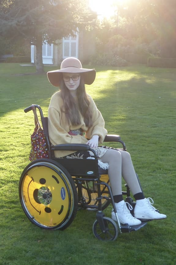 Image of Sakara using her wheelchair in a grassy park.