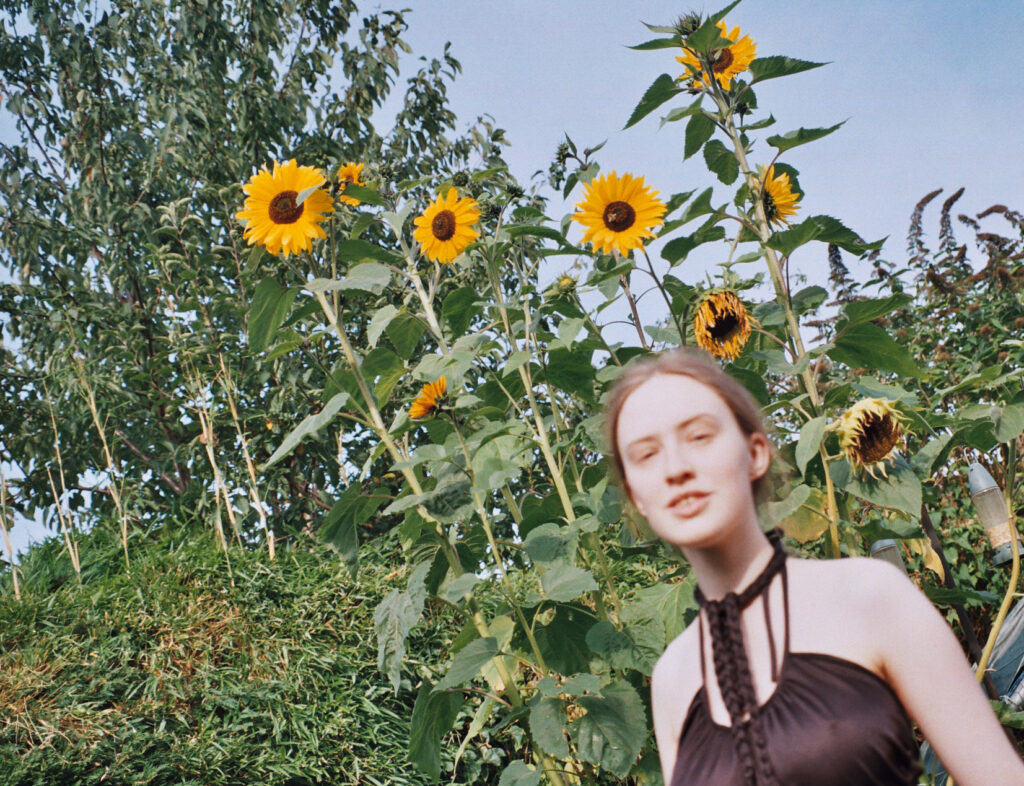 Photo of sakara wearing a black top standing in front of some sunflowers.